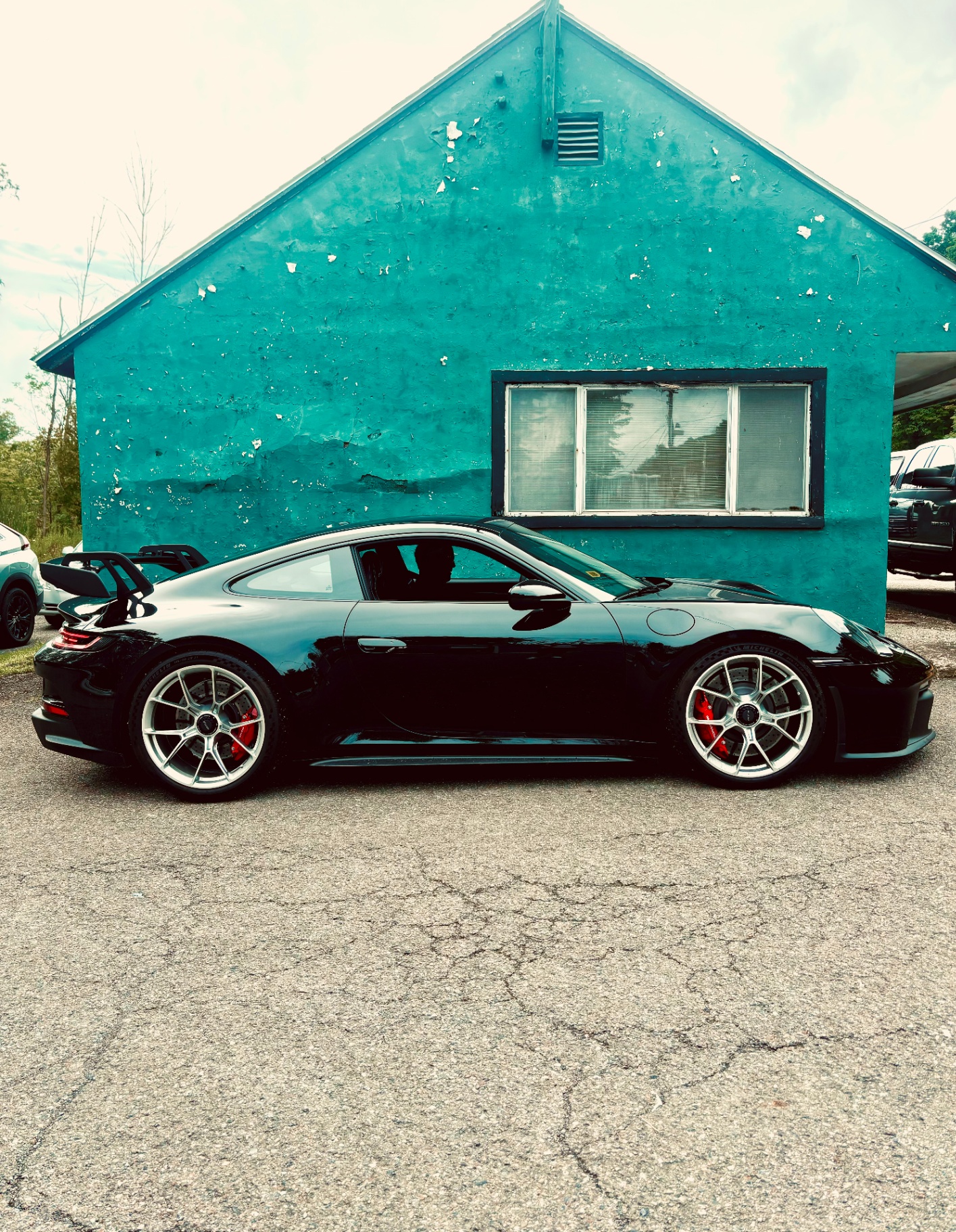 Black Porsche 911 GT3 Touring in profile parked in front of a weathered teal building