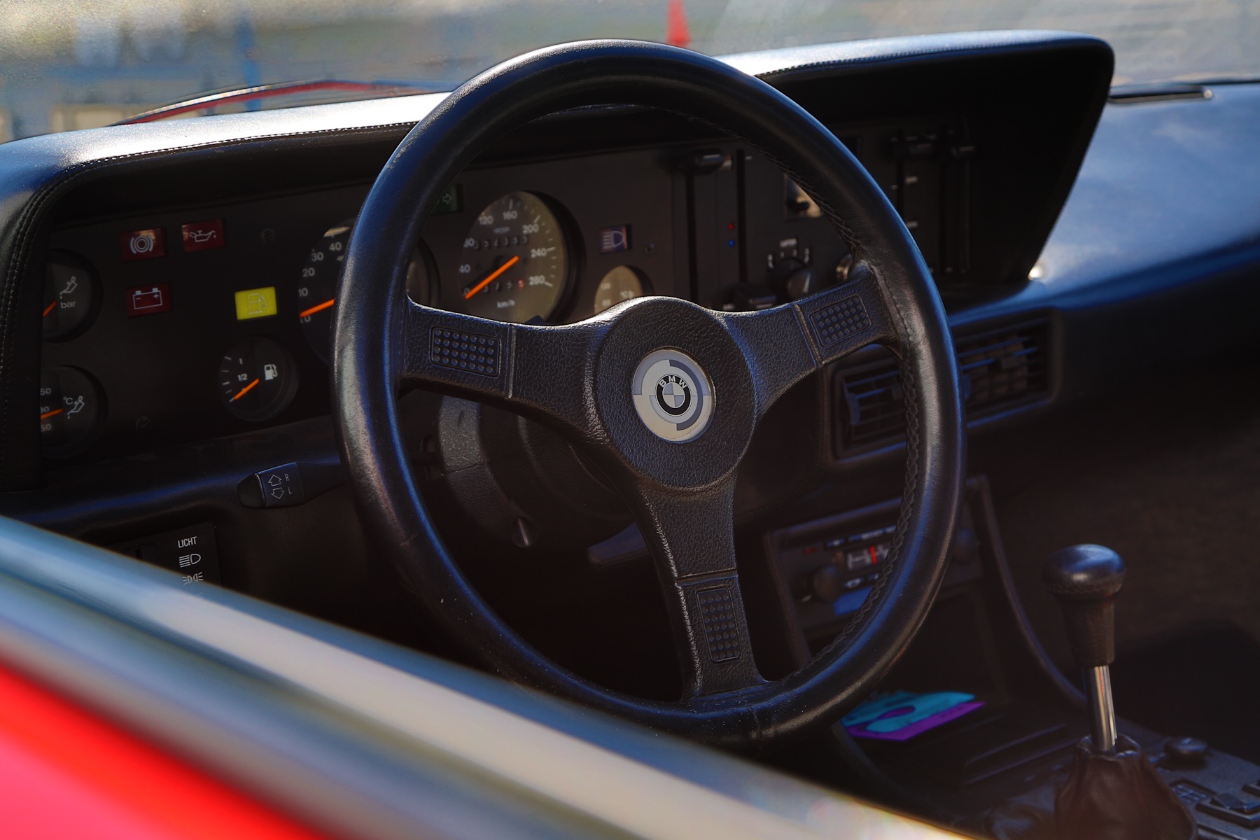 BMW analog gauge cluster and three-spoke steering wheel viewed through the driver's window